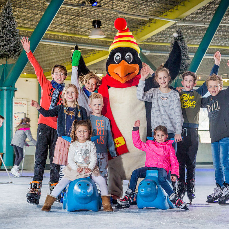 Kinderen juichen op het ijs naast de pinguïn-mascotte van Triavium