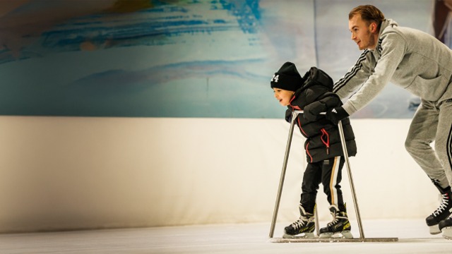 Kleuter leert schaatsen met een rekje, geholpen door een begeleider